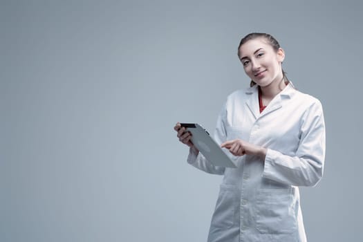 Young female scientist wearing a lab coat is using a digital tablet, looking at the camera and smiling, suggesting confidence and expertise in scientific research