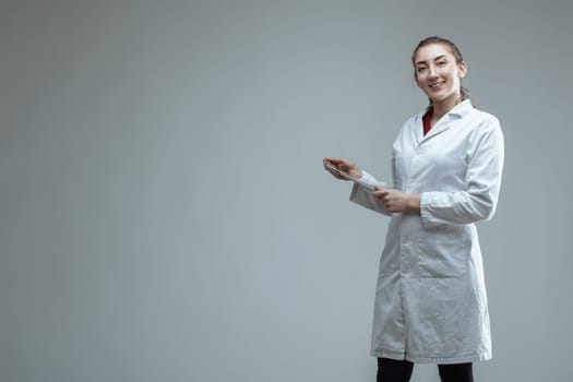 Young female scientist wearing a lab coat is holding a digital tablet, smiling at the camera, suggesting expertise in science, research, and engineering