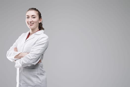 Portrait of a confident young female scientist smiling with crossed arms in a studio setting against a gray background, embodying professionalism and expertise in research