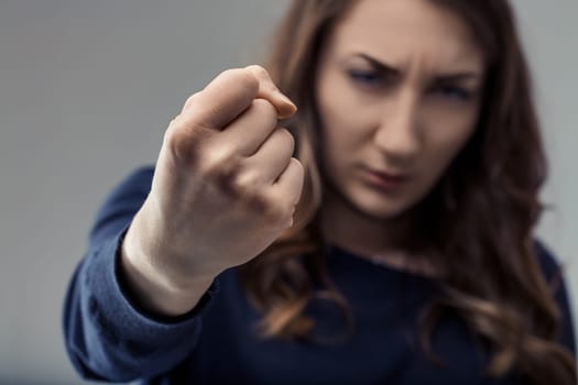 Young woman displaying her fist, radiating anger and determination, prepared to fight for her rights against a muted gray background, embodying strength and defiance