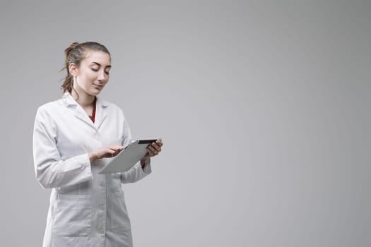 Young female scientist wearing lab coat using digital tablet, conducting research in a laboratory setting, focused on scientific innovation and technological advancement
