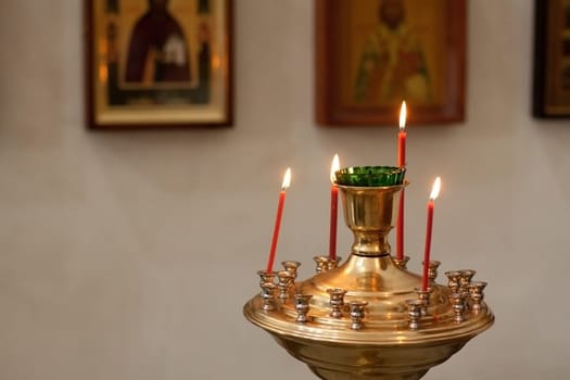 Lit candles in ornate metal holder with religious icons in background.