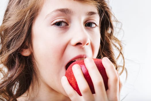 Close-up portrait of a young girl joyfully taking a large bite out of a ripe red apple, savoring a nutritious and delicious snack filled with natural sweetness