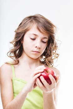 Young girl with curly brown hair holding a shiny red apple, gazing thoughtfully at the fruit against a clean white background, embodying curiosity and innocence