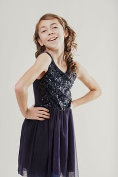 Cheerful preteen girl wearing a sparkling sequined dress, posing confidently with hands on her hips and radiating joy through her bright smile in a studio setting