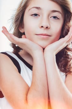 Charming young girl with delicate features and captivating blue eyes, posing with her chin resting gently on her hands, exuding a sense of innocence and tranquility