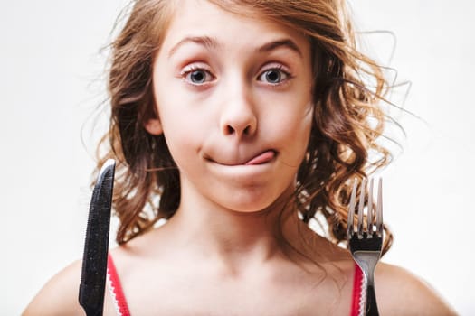 Child eagerly awaiting a meal, holding a fork and knife with a playful expression, tongue peeking out, capturing a moment of joyful anticipation and innocence