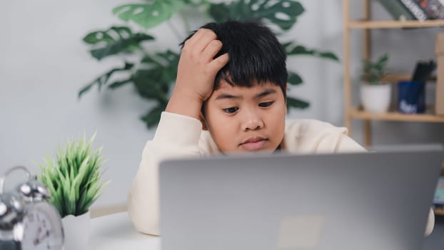 Little Asian boy sitting alone and looking out with a bored face, Preschool child laying head down on the table with sad bored with homework, Spoiled child.