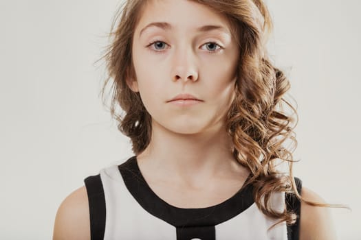 Portrait of a serious young girl with long, wavy brown hair, gazing directly at the camera against a clean, white background, capturing a moment of contemplation and innocence