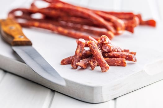 Smoked kabanos. Mini dried thin sausages on cutting board on a white table.