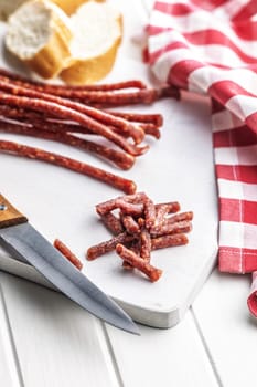 Smoked kabanos. Mini dried thin sausages on cutting board on a white table.