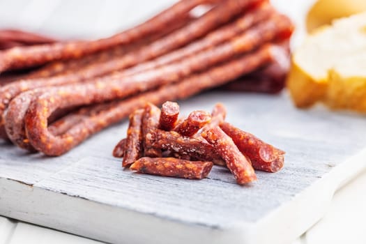 Smoked kabanos. Mini dried thin sausages on cutting board on a white table.