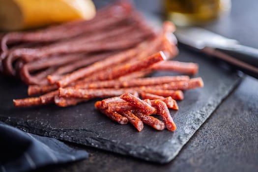 Smoked kabanos. Mini dried thin sausages on cutting board on a black table.