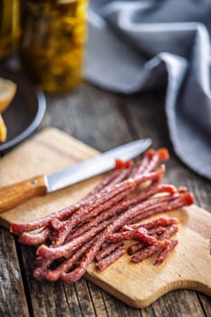 Smoked kabanos. Mini dried thin sausages on cutting board on a wooden table.