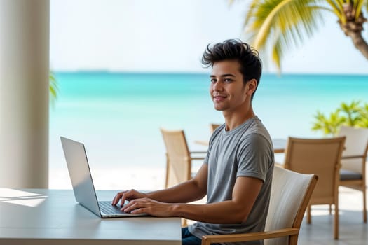 Young man sitting at a table with a laptop in a tropical beachside setting overlooking crystal-clear waters. Concept of remote work, modern business lifestyle, and freedom in paradise