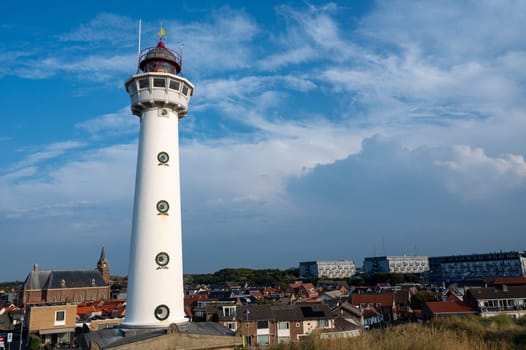 The approx. 28 m high white lighthouse J.C.J. van Speijk in Egmond aan Zee, North Holland, Netherlands with some of the town's houses