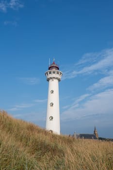 The approx. 28 m high white lighthouse J.C.J. van Speijk in Egmond aan Zee, North Holland, Netherlands with the Catholic St. Agnes Church, beach grass and sand dunes