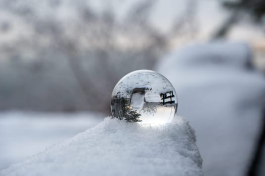 Glass ball lying in the snow on a cold winter day, with reflections of snow-covered landscape in the glass