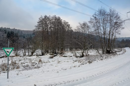 Winter landscape with lots of snow, trees, dirt road and a sign with the inscription "Nature reserve"" in German"