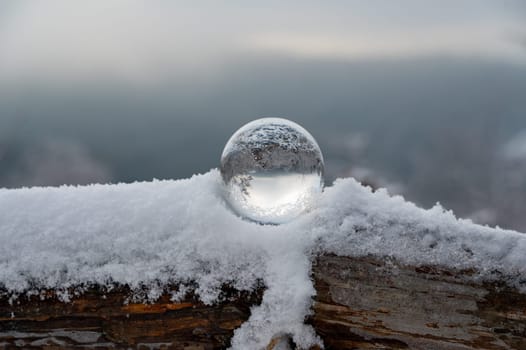 Glass ball on a wood on a cold winter day, with reflections of trees and snow in the glass
