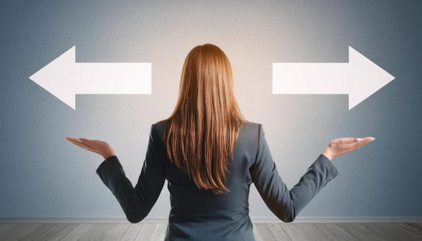 Rear view doubtful businesswoman in a suit balancing hands as stands in front wall with arrows pointing two different directions. Difficult business choice between left and right sides