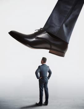 Tiny man office worker standing under pressure of the giant shoe of his big boss about to step on him. Workplace confrontation, leadership concept. Power dynamics or intimidation in business