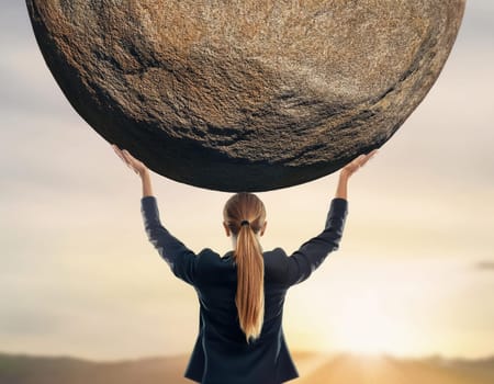 Businesswoman lifting and holding a big boulder above head. Solving an immense business task, symbol of strength and perseverance. Standing up to troubles, burden concept