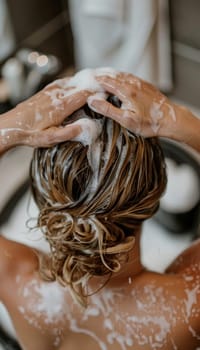 Close-up view of a person's hands gently massaging shampoo into wet, dark hair, creating a calming, therapeutic experience