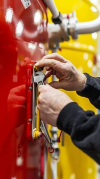 Closeup of a plumber's hands using a wrench to adjust or tighten a metal pipe, with a red tool box and other equipment in the background