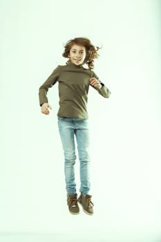 Young girl with long brown hair is captured mid-air, her joyful expression radiating pure happiness as she jumps with carefree abandon against a clean white backdrop