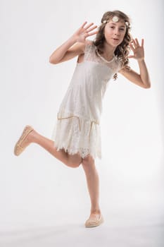 Young girl with a flower crown is playfully dancing and expressing joy, wearing a white lace dress against a white background, creating a light and airy image