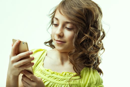 Portrait of a smiling preteen girl with curly, brown hair, holding a smartphone and engaging with the screen, set against a clean white background