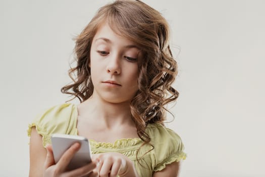 Elementary age girl with curly hair holding a smartphone and looking at the screen with a focused, pensive expression, suggesting concentration or contemplation