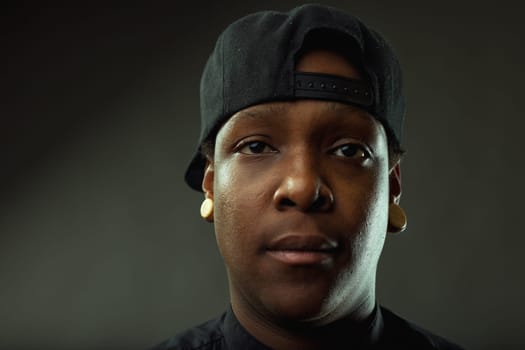 Close-up portrait of a serious young african american man wearing a baseball cap and plugs. Staring intensely at the camera against a dark background. Conveying a sense of confidence and urban style