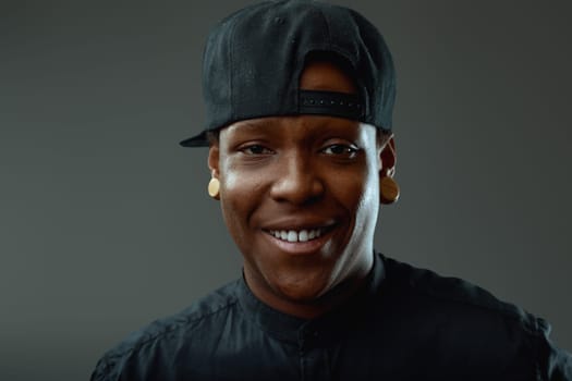 Studio portrait of a cheerful young african american man wearing a baseball cap and black shirt, smiling confidently at the camera against a gray background