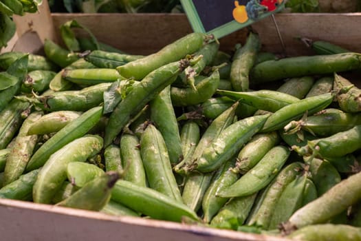 A box of green peas is displayed in a market. The peas are fresh and ready to be eaten