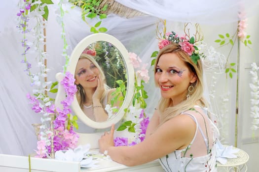A pretty elf with flowers in her hair sits in front of an enchanted mirror