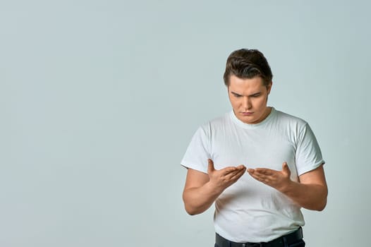 a man standing on a gray background smiles cheerfully with open arms as a sign of friendly greeting. High quality photo