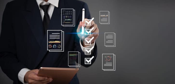 Business professional in a suit uses a digital checklist and tablet to review documents, charts, and data, symbolizing organized project management and efficient task completion.