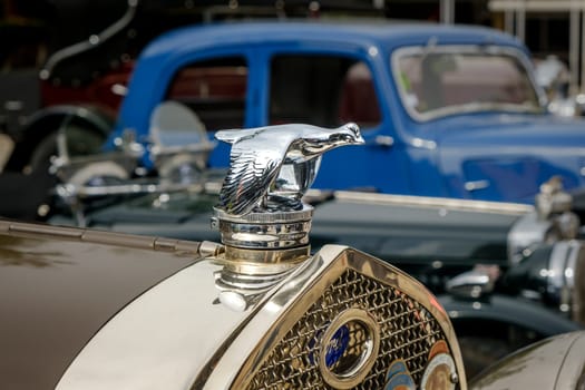 Lisbon, Portugal - Oct 15, 2023: Close-up and selective focus of flying quail bird bonnet mascot on top of hood or bonnet and Ford emblem and logo plate on grille. Radiator cap used only on Ford Model A in 1930s.