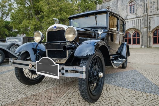 Lisbon, Portugal - Oct 15, 2023: Front view of Ford Model A or A-Model Ford or the A and A-bone in original green color parked on cobblestone road near other oldtimers during annual Classic Car Owners meeting.