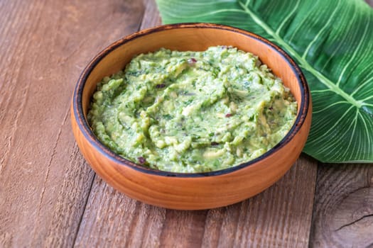 Wooden bowl of creamy guacamole on a rustic wooden table with a large green leaf