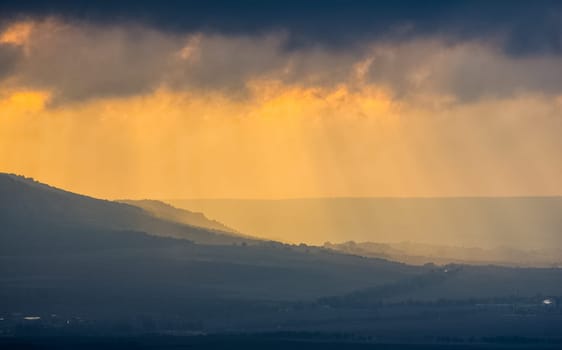 Dawn in the mountains of Crimea. A light haze of mist over the mountains and rays of the sun through the clouds.