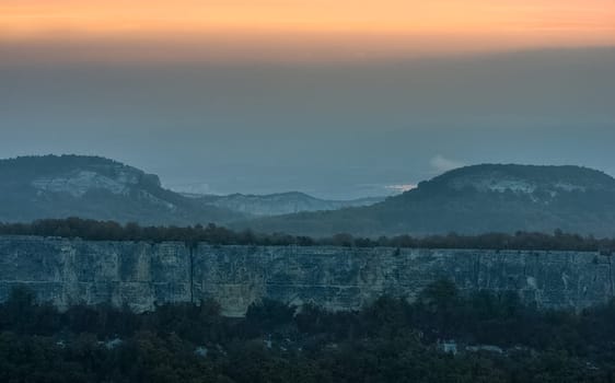 Dawn in the mountains of Crimea. A light haze of mist over the mountains and rays of the sun through the clouds.