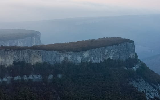 Dawn in the mountains of Crimea. A light haze of mist over the mountains and rays of the sun through the clouds.