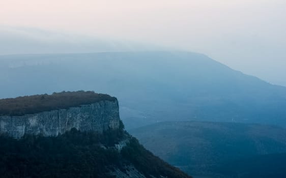 Dawn in the mountains of Crimea. A light haze of mist over the mountains and rays of the sun through the clouds.