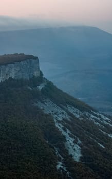 Dawn in the mountains of Crimea. A light haze of mist over the mountains and rays of the sun through the clouds.