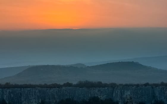 Dawn in the mountains of Crimea. A light haze of mist over the mountains and rays of the sun through the clouds.