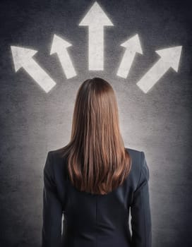 Rear view puzzled businesswoman facing a wall with multiple illuminated arrows pointing up. Decision making moment as choosing the relevant path in career