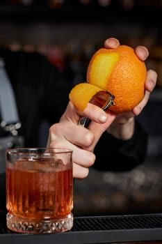 bartender makes a cocktail in a glass with orange peel at the bar